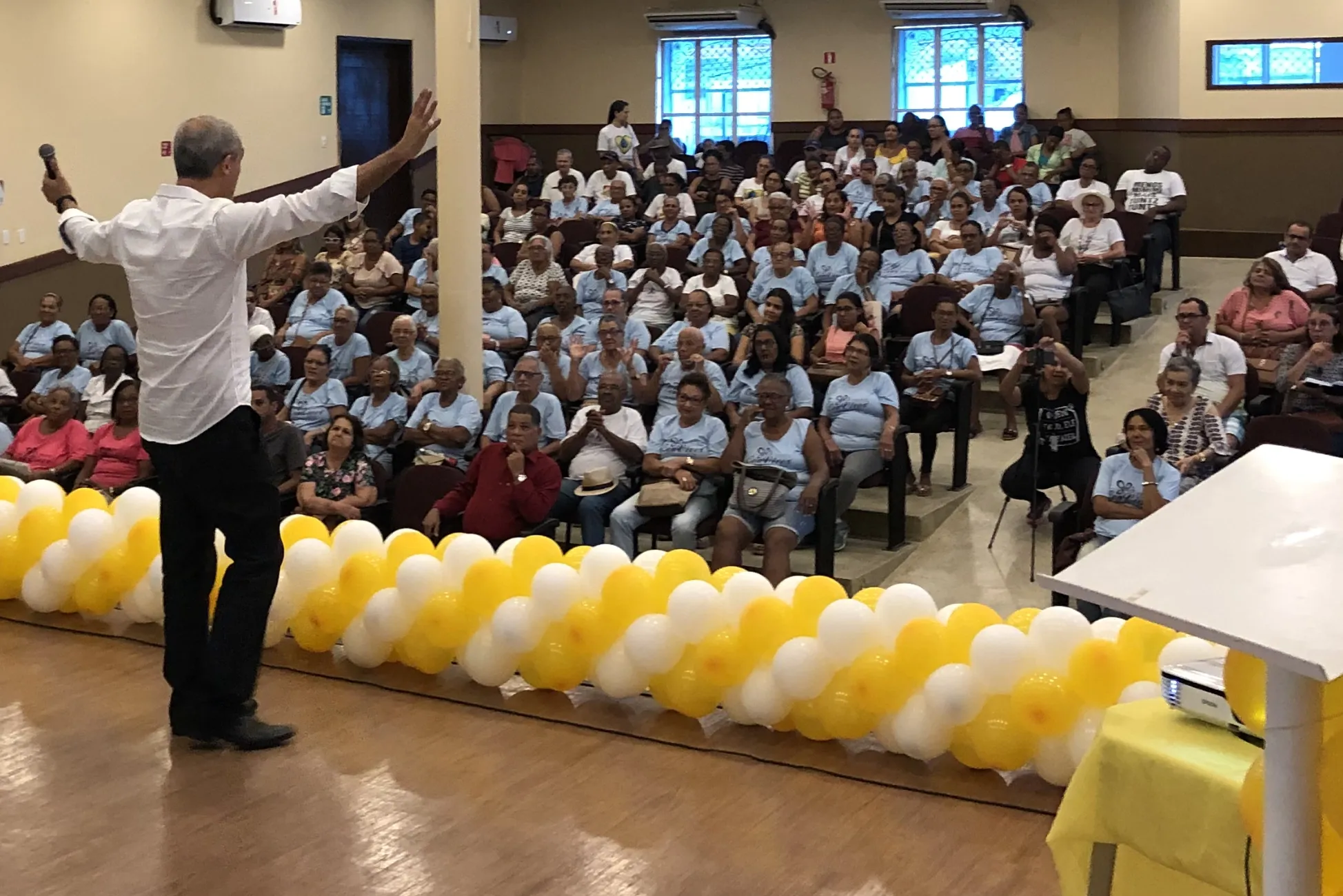 Weber Jatahy no palco, de braços abertos, diante de uma plateia